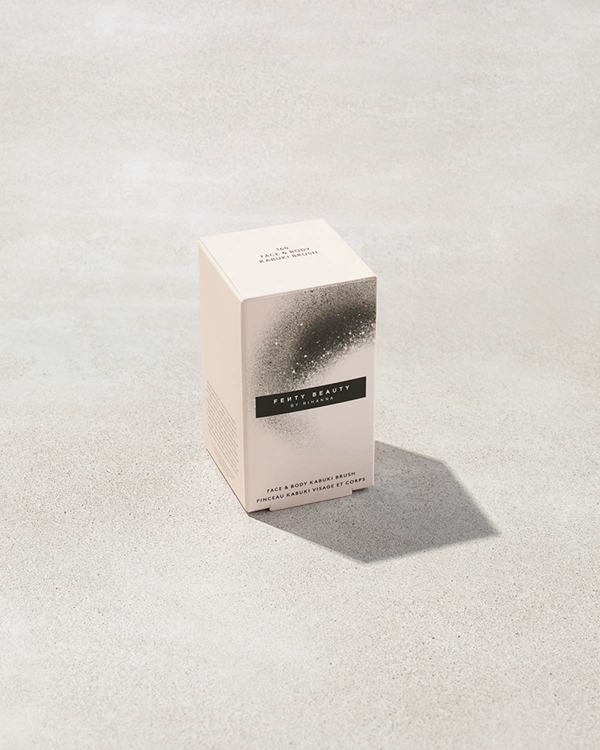 The packaging for a fenty face and body kabuki brush with pink bristles on a gray background.