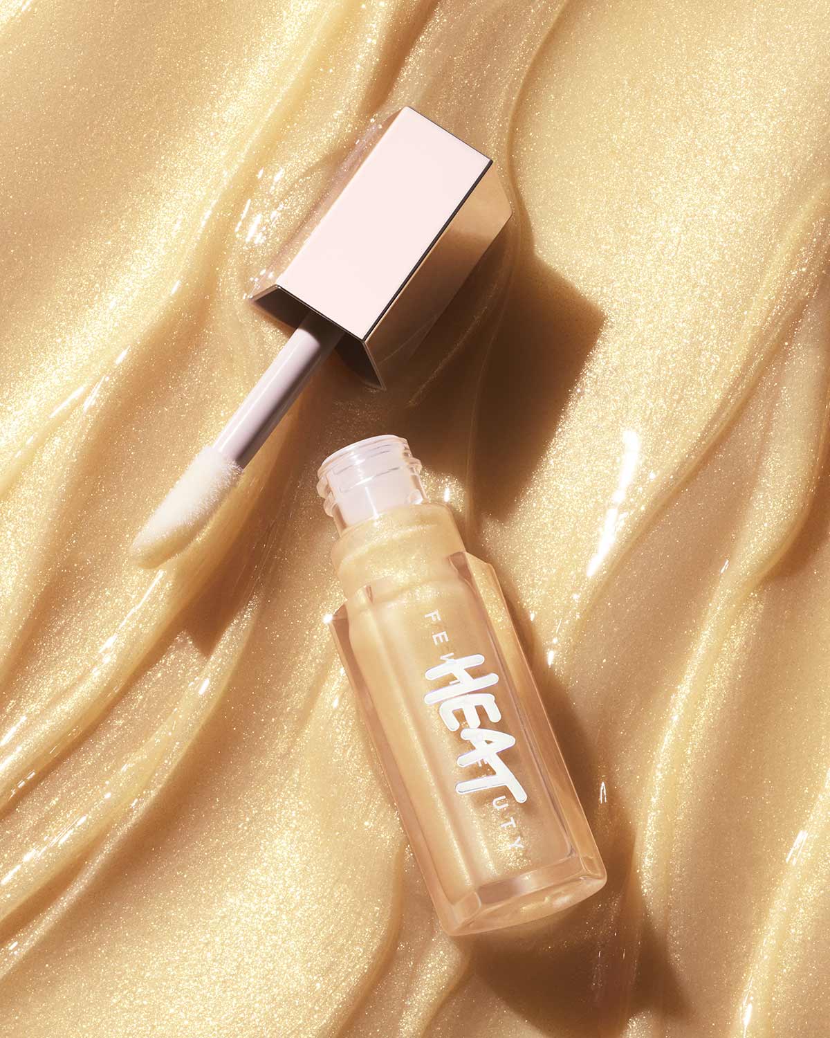 A closed tube of Gloss Bomb Heat Luminizer + Plumper with the lip gloss texture in the background.