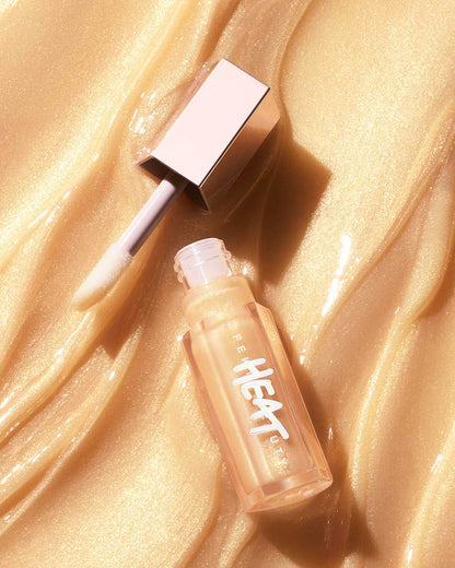 A closed tube of Gloss Bomb Heat Luminizer + Plumper with the lip gloss texture in the background.