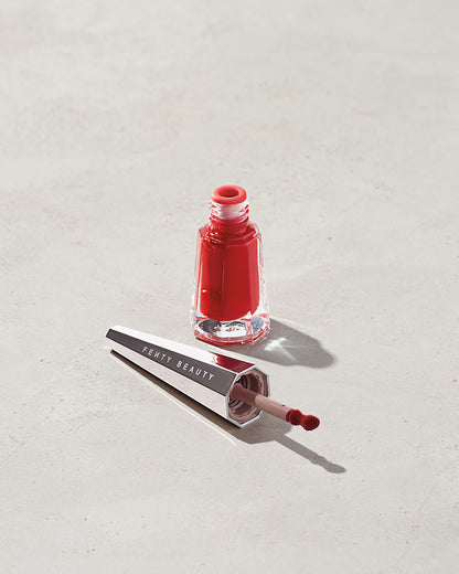 Jar of lip paint with the lid applicator laying next to it on a gray background