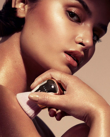 A woman holding a fenty face and body kabuki brush against her shoulder