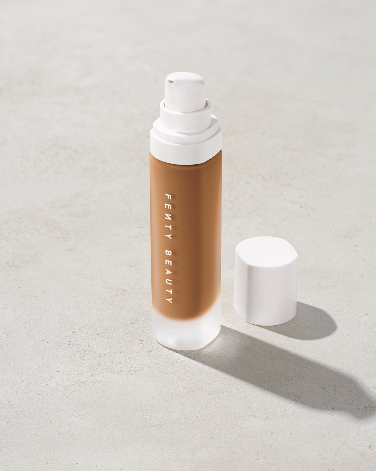 open bottle of Fenty Beauty Pro Filt'r Soft Matte Longwear Foundation with pump dispenser in shade 385 on concrete background