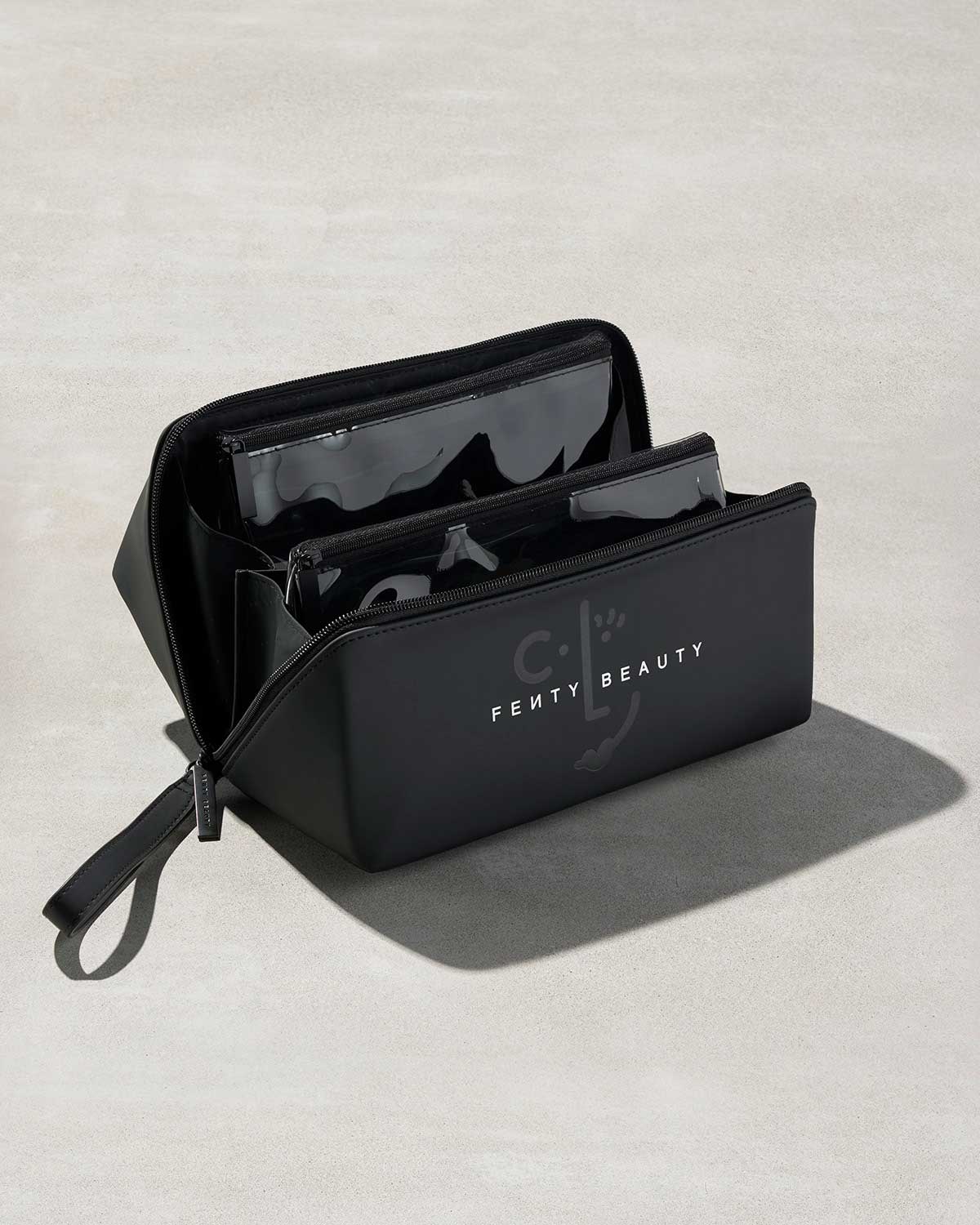 One open black rectangular bag with fenty branding, showing two triangular clear bags nestled inside it.