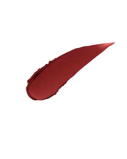 A smear of Fenty Icon Velvet lipstick in brick red color on a light background.