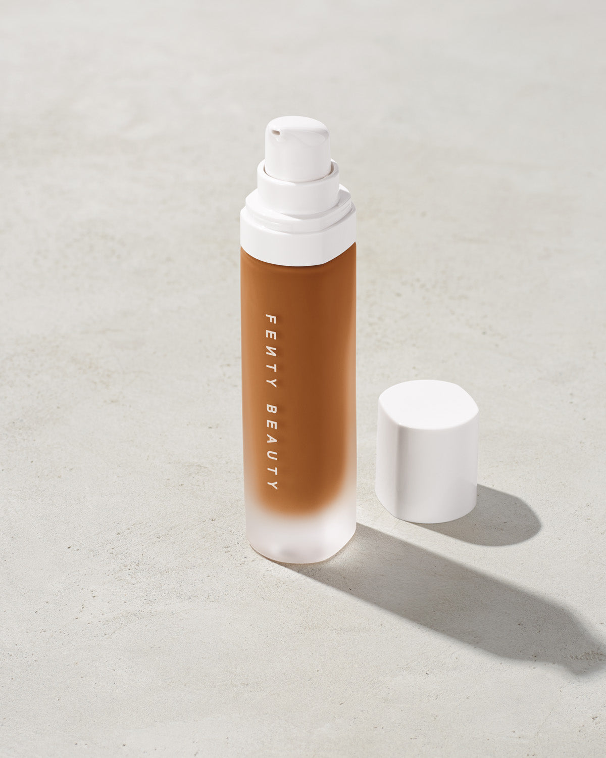 open bottle of Fenty Beauty Pro Filt'r Soft Matte Longwear Foundation with pump dispenser in shade 440 on concrete background