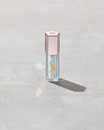 Closed tube of Gloss Bomb Heat lip gloss and plumper in the shade Glass Slipper on a grey background.