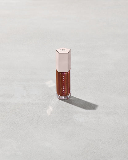 A close tube of Gloss Bomb Universal Lip Luminizer in the shade Hot Chocolit Fantasy on a grey background.