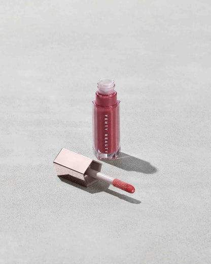 An open tube of Gloss Bomb Universal Lip Luminizer in the shade RiRi on a grey background.