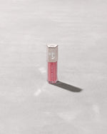 A closed tube of Gloss Bomb Universal Lip Luminizer in the shade Candy Soda on a grey background.