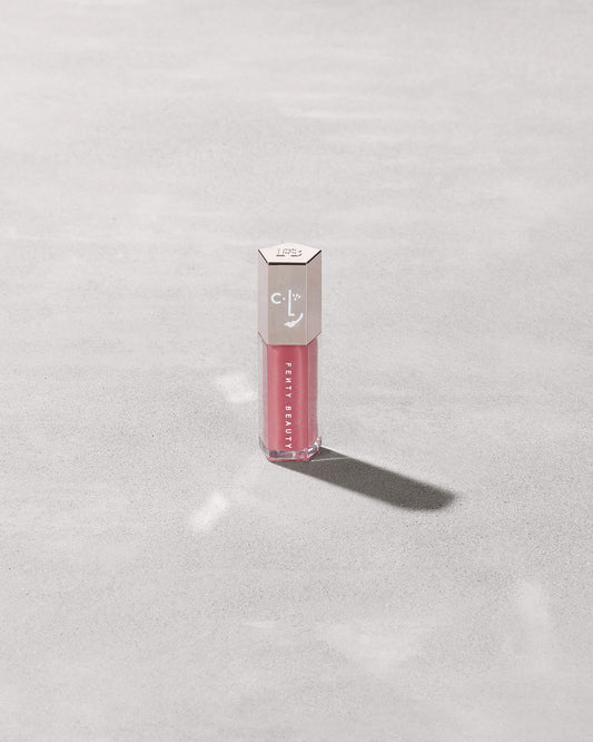 A closed tube of Gloss Bomb Universal Lip Luminizer in the shade Candy Soda on a grey background.
