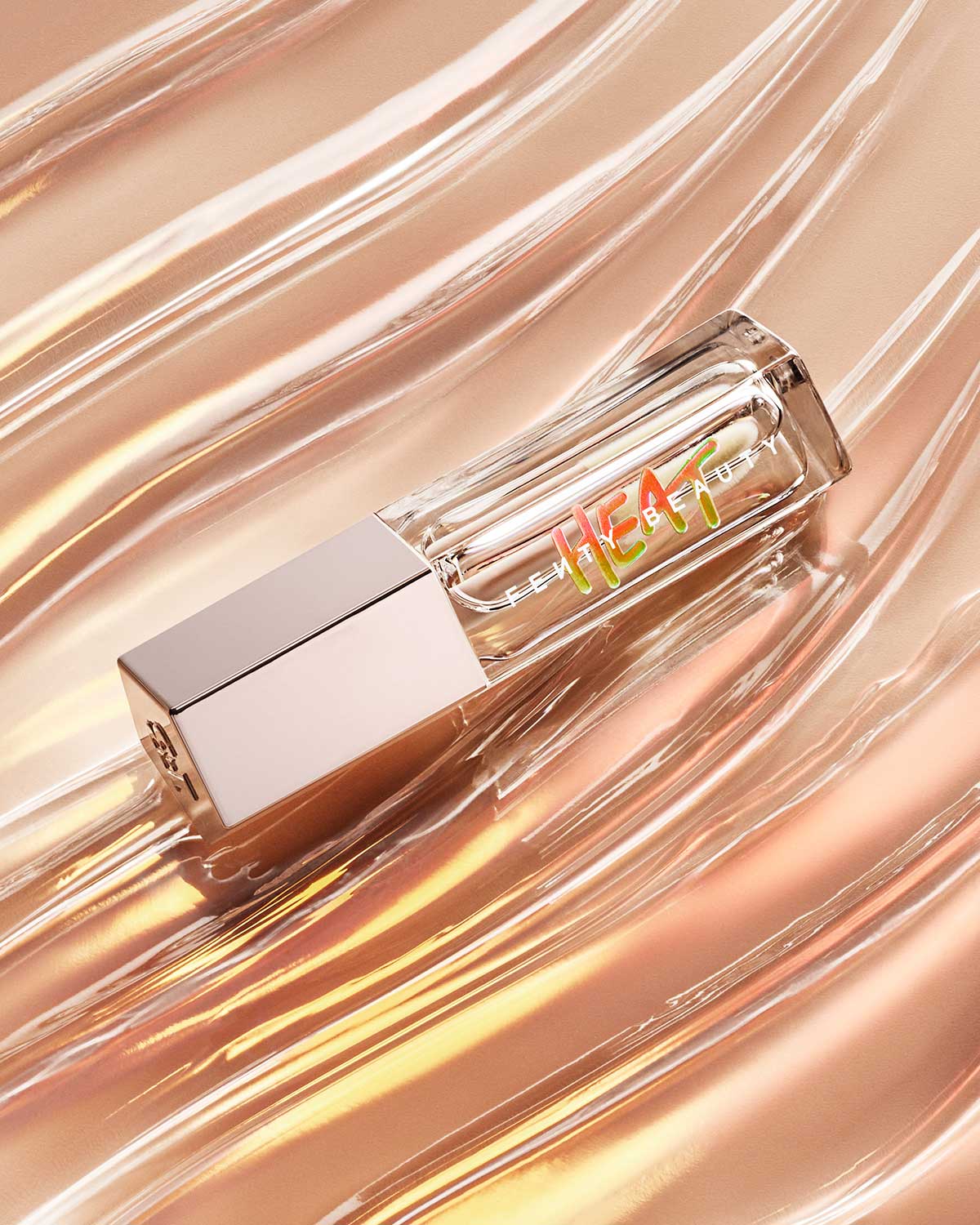 A closed tube of Gloss Bomb Heat Luminizer Plus Plumper with the lip gloss texture in the background.