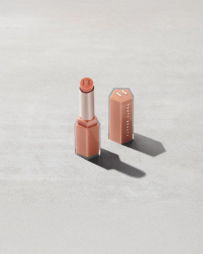 Open product shot of Gloss Bomb Stix Shimmer in shade Fenty Glow on a concrete background.