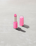 Open product shot of Gloss Bomb Stix Shimmer in shade Flamingo Fling on a concrete background.