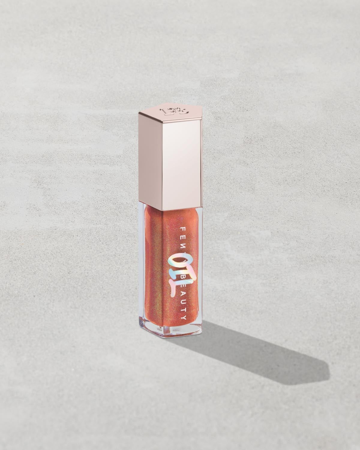 Gloss Bomb Oil Luminizing Oil and Gloss in shade Fenty Glow product against a concrete background.