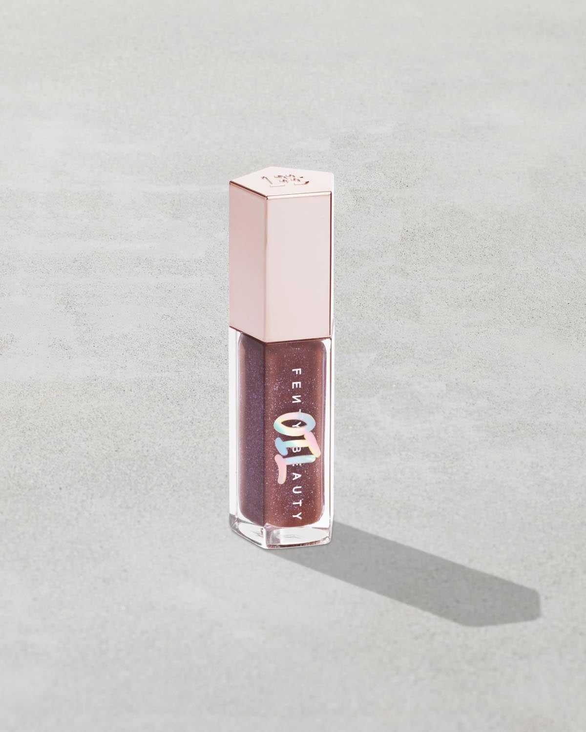 Gloss Bomb Oil Luminizing Oil and Gloss in shade Rose Amber product against a concrete background.