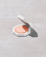 Open product shot of Demi'glow Light-Diffusing Highlighter in shade Tutu Much on a concrete backdrop.