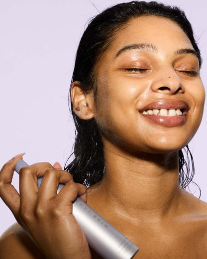 Woman applying face mist to her face with a white background