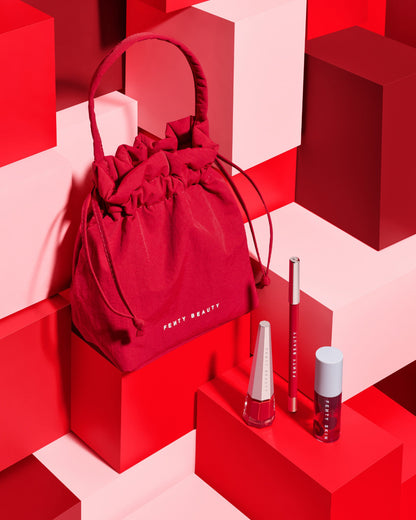 Editorial shot of Cherry Mouth 3-Piece Lip Set includes Stunna Lip Paint, Traced Out Lip Pencil Liner, and Fenty Treats Lip Oil with an exclusive cherry red Fenty Beauty pouch.